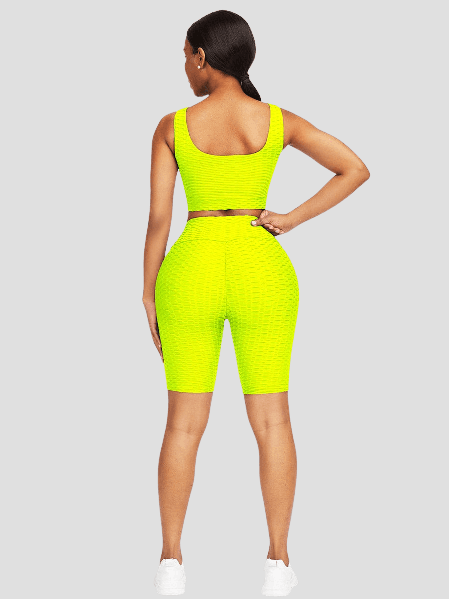 Woman standing backwards wearing a yellow mid-thigh shorts and sports bra activewear set with a honeycomb pattern.