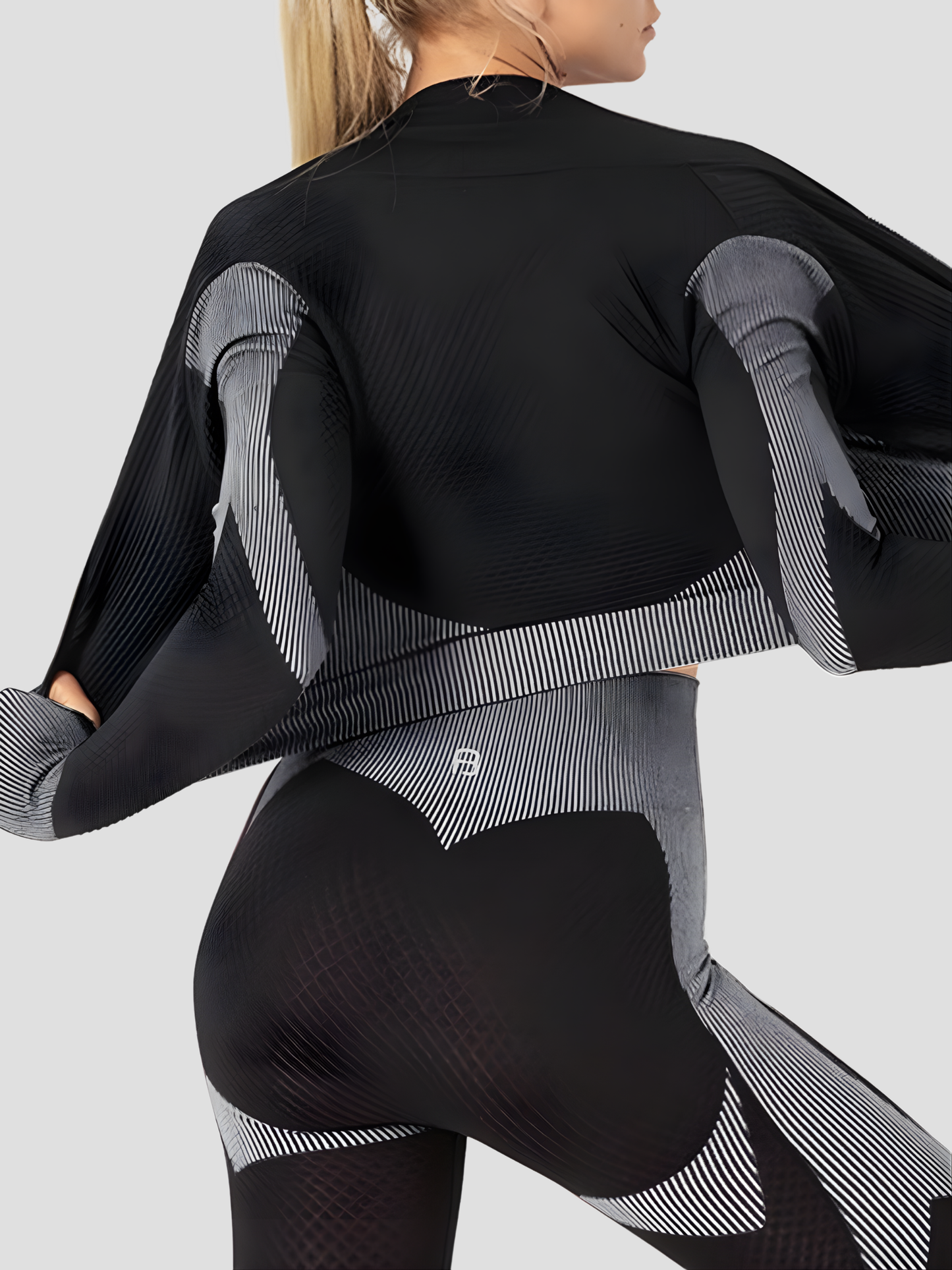 Woman wearing a black and gray color block activewear BBL jacket with matching leggings.