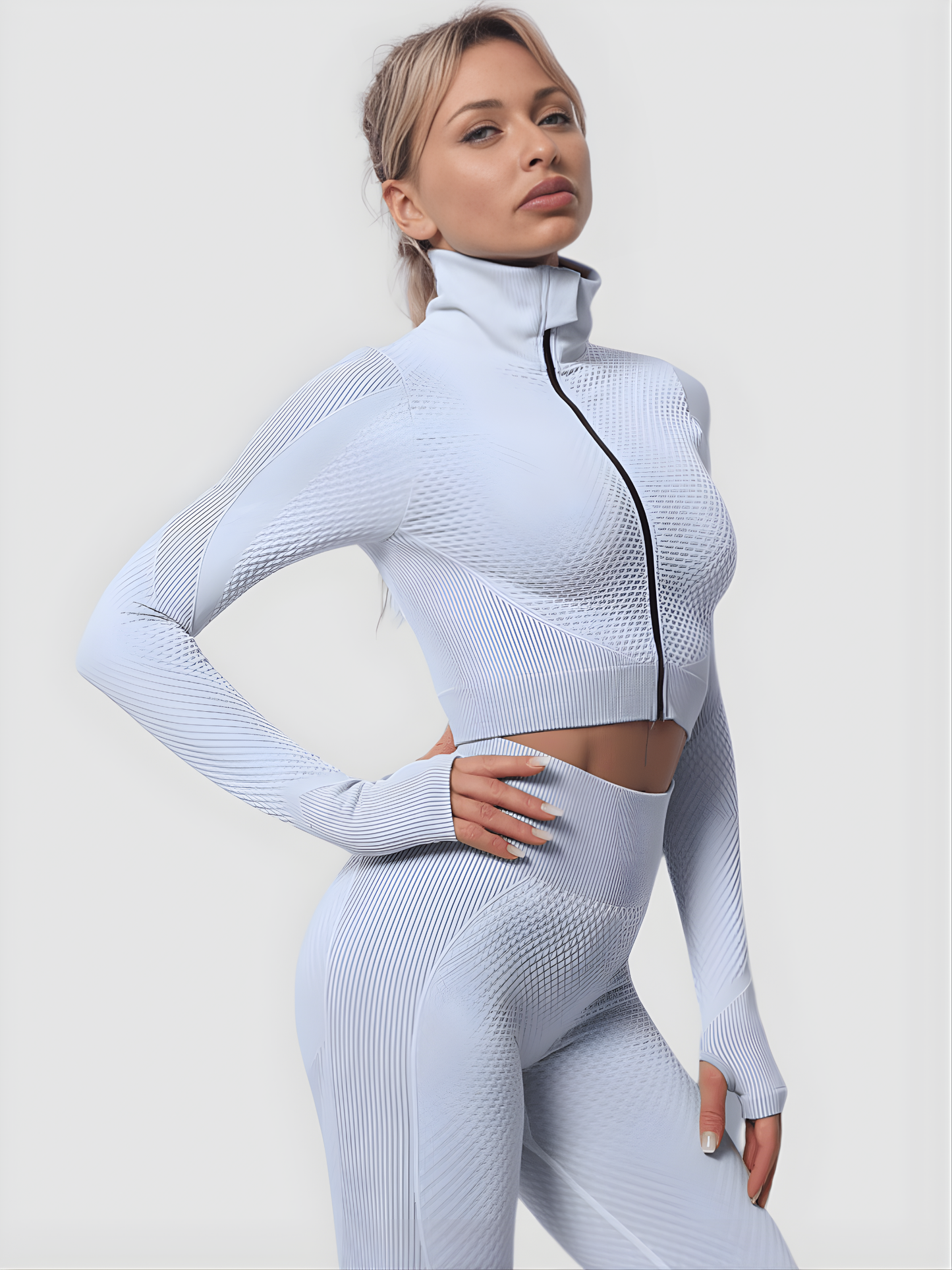 Woman wearing a silver gray zippered cropped activewear BBL jacket and matching leggings.