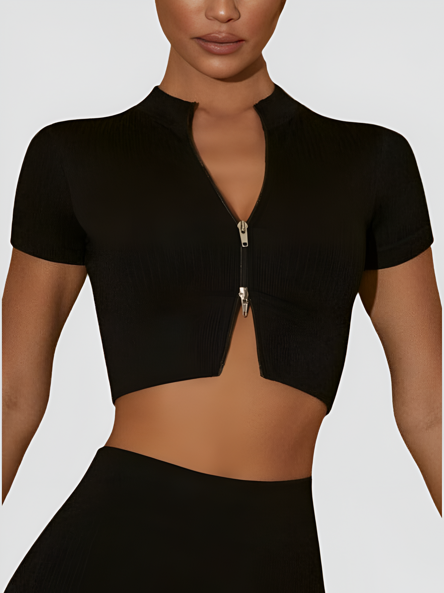 Woman wearing a black cropped ribbed activewear top with a double zipper and short sleeves by BodyFlexx.