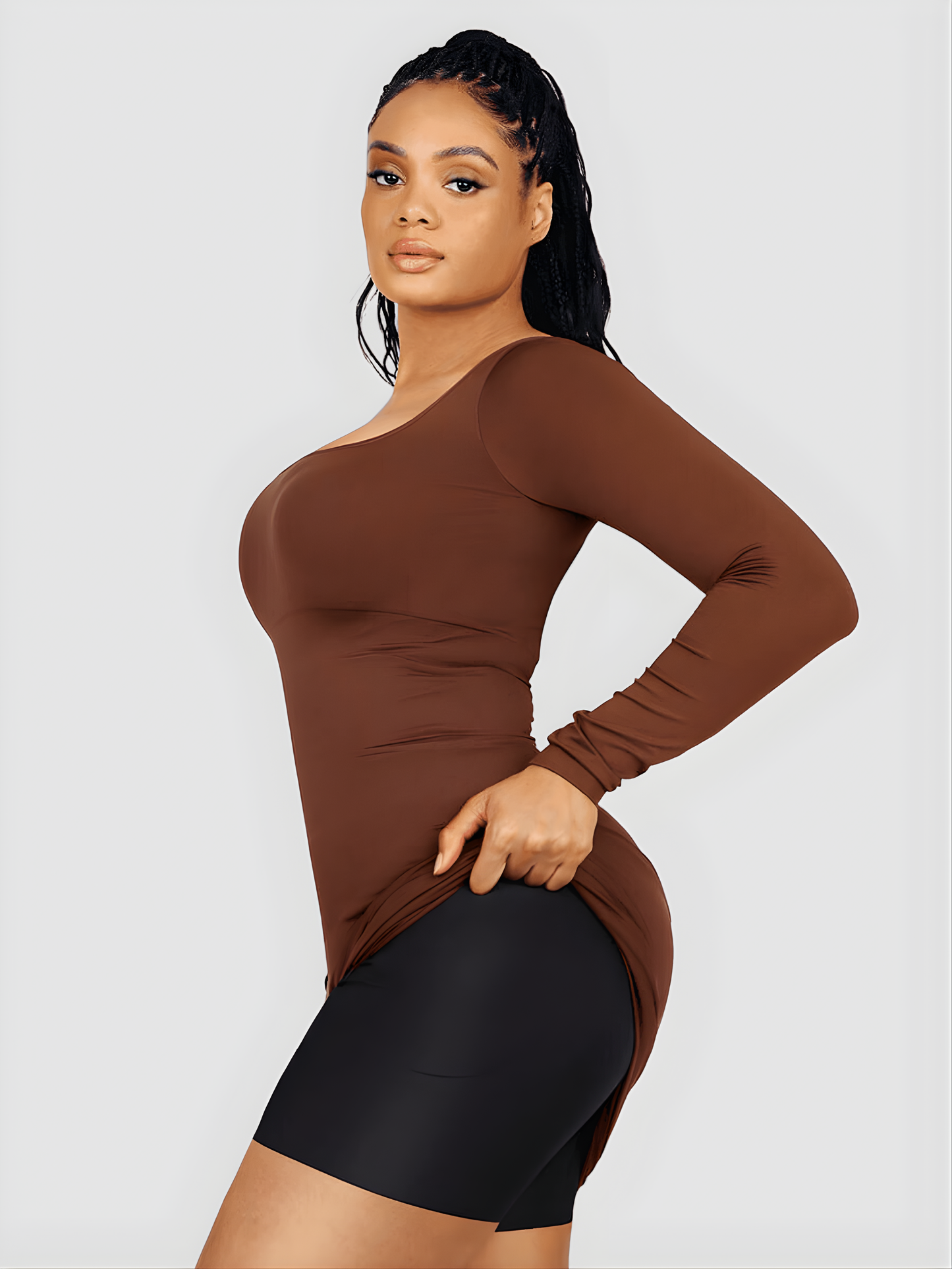 Woman lifting up a brown long-sleeve top dress to show her seamless shapewear with removable hip pads by Bodyflexx.