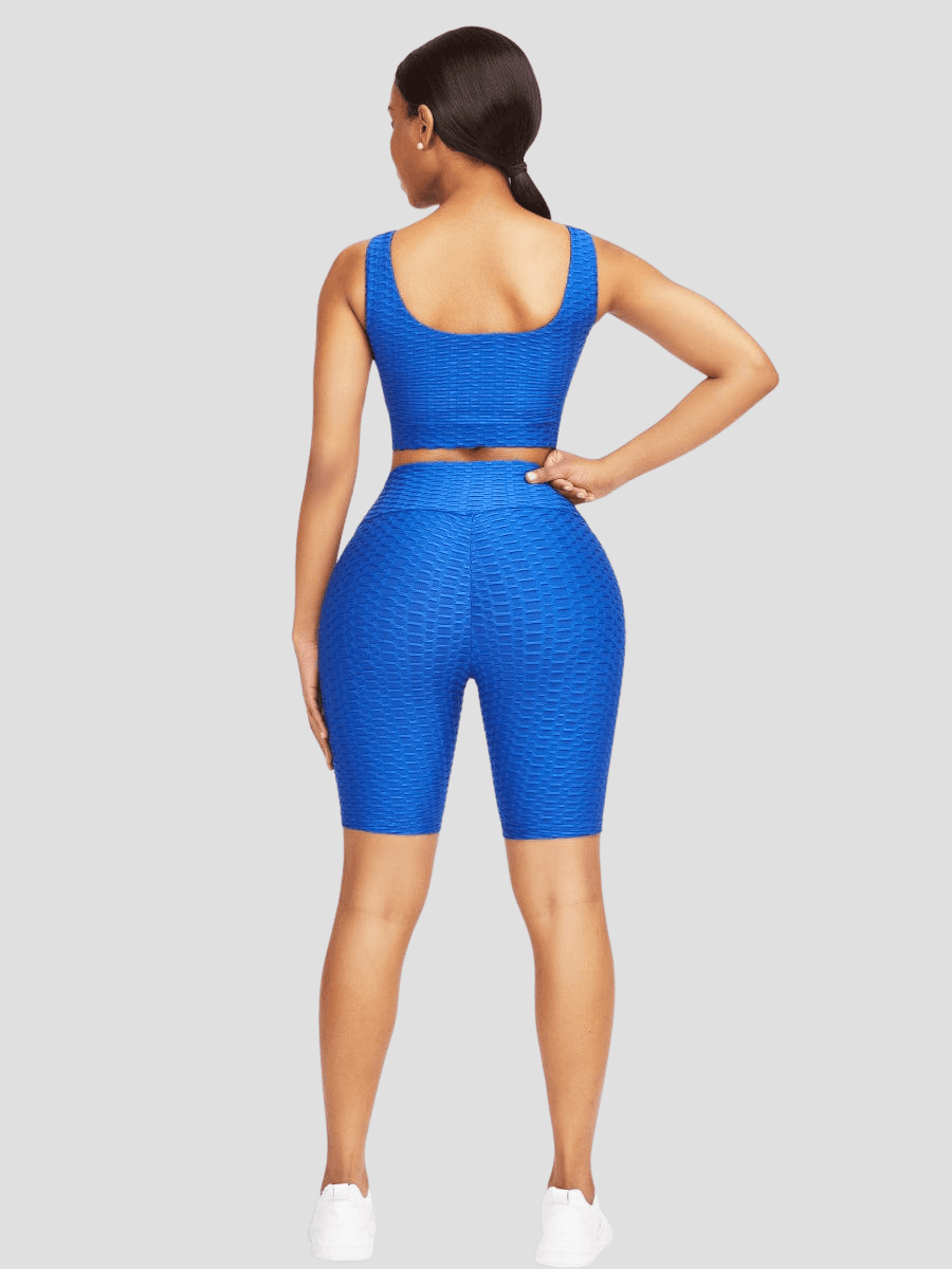 Woman standing backwards wearing a blue mid-thigh shorts and sports bra activewear set with a honeycomb pattern.