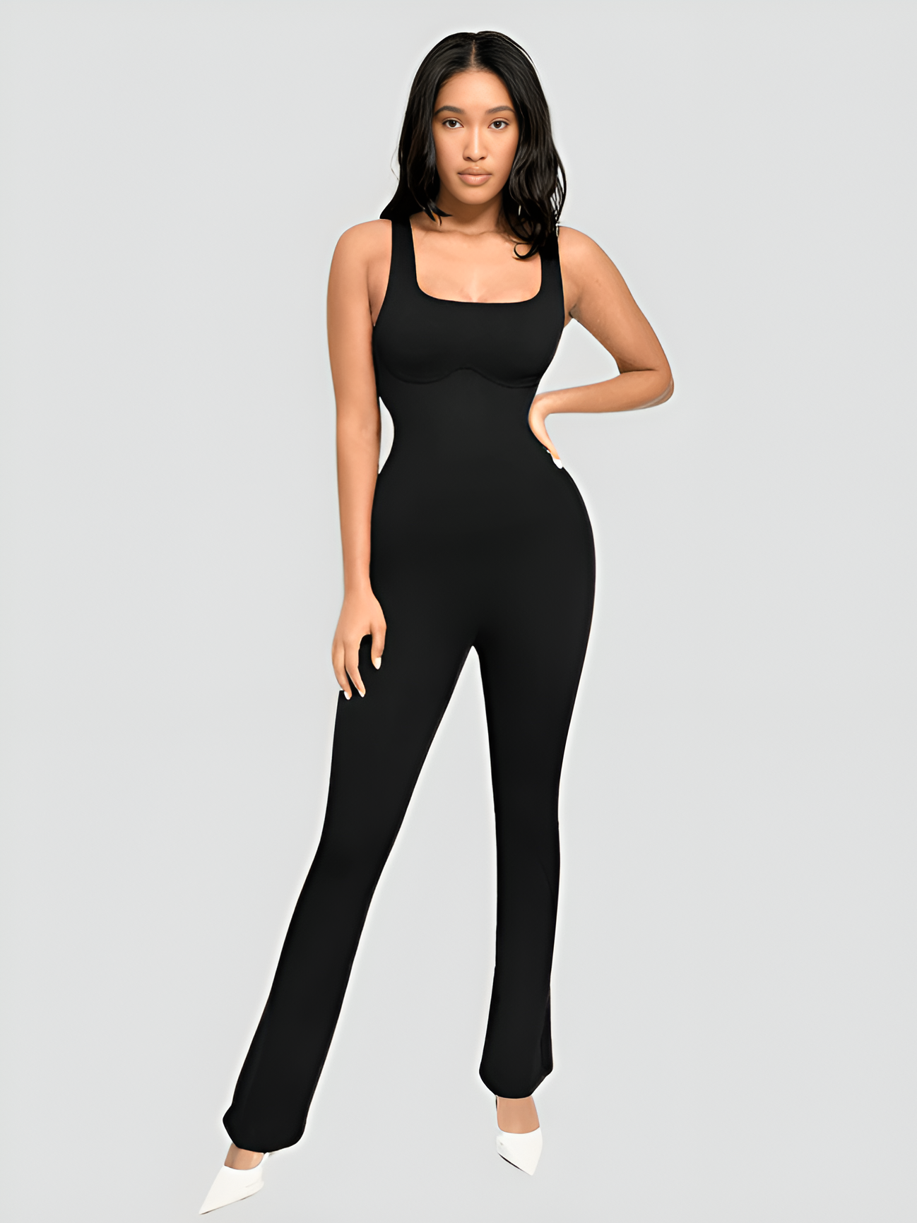 Woman posing wearing a black sleeveless flared jumpsuit romper with a  built-in shapewear panel and a square neckline.