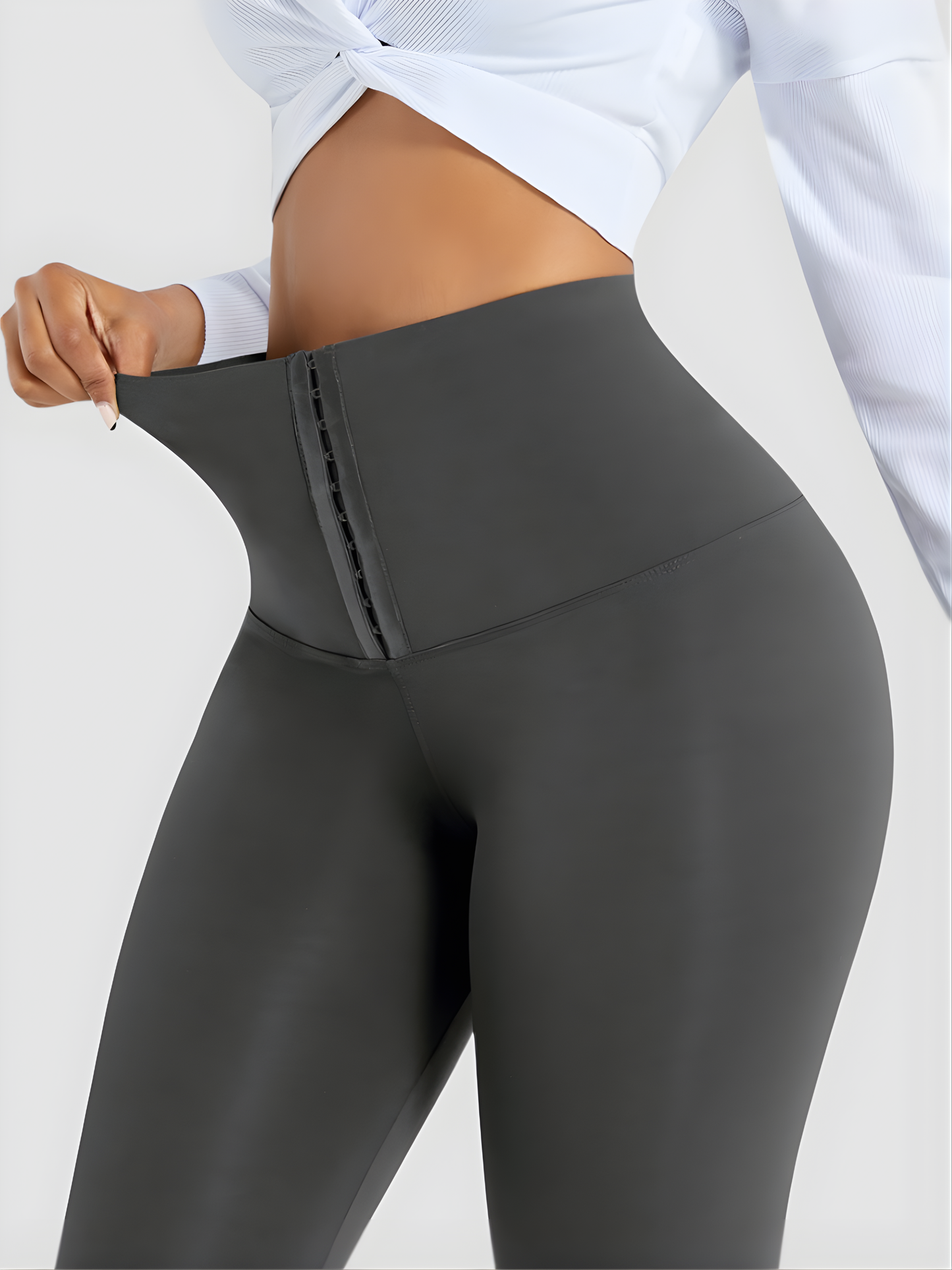 Woman posing wearing gray waist training corset leggings by BodyFlexx Shapewear and a white blouse.