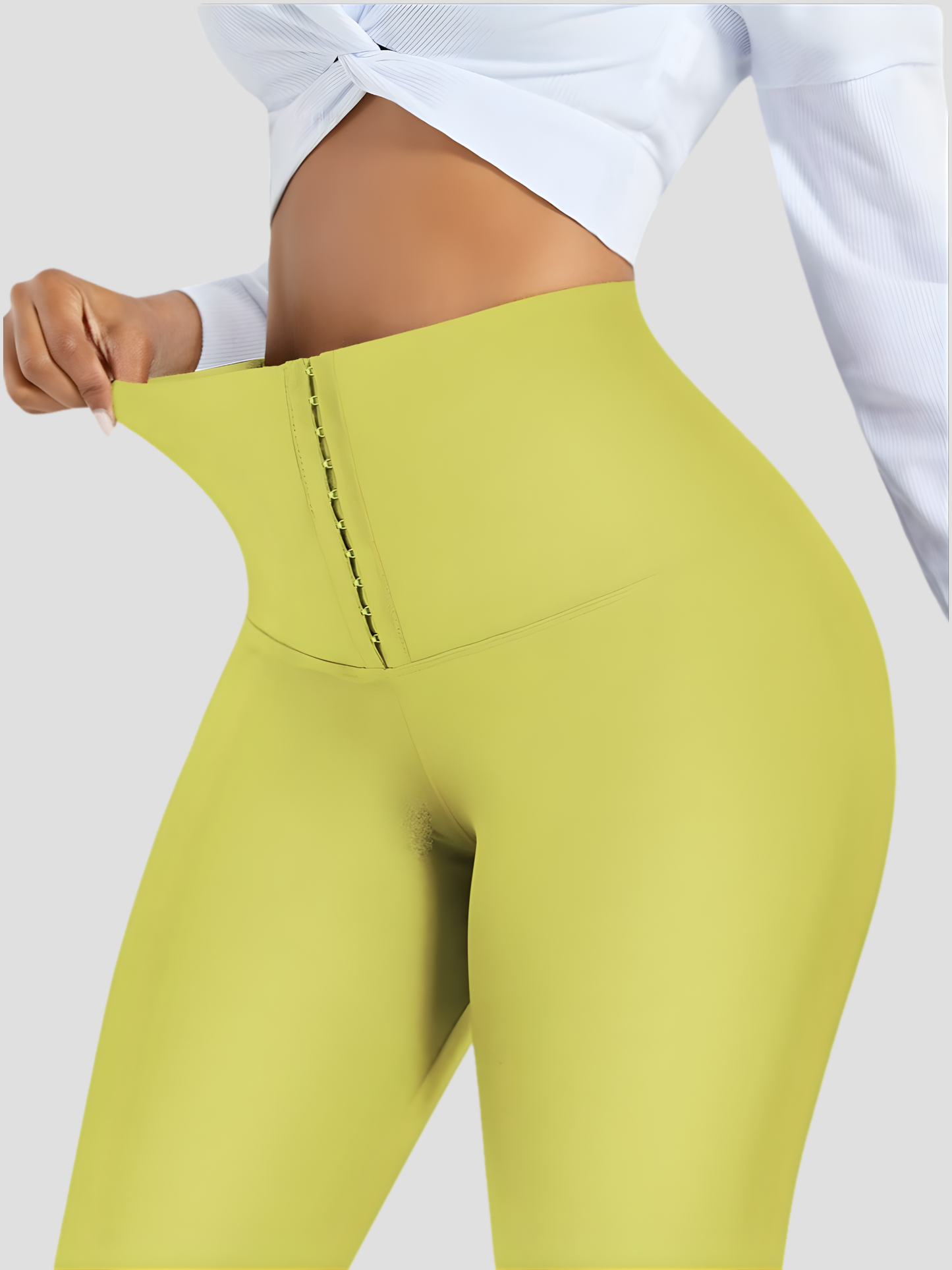 Woman posing wearing yellow waist training corset leggings by BodyFlexx Shapewear and a white blouse.