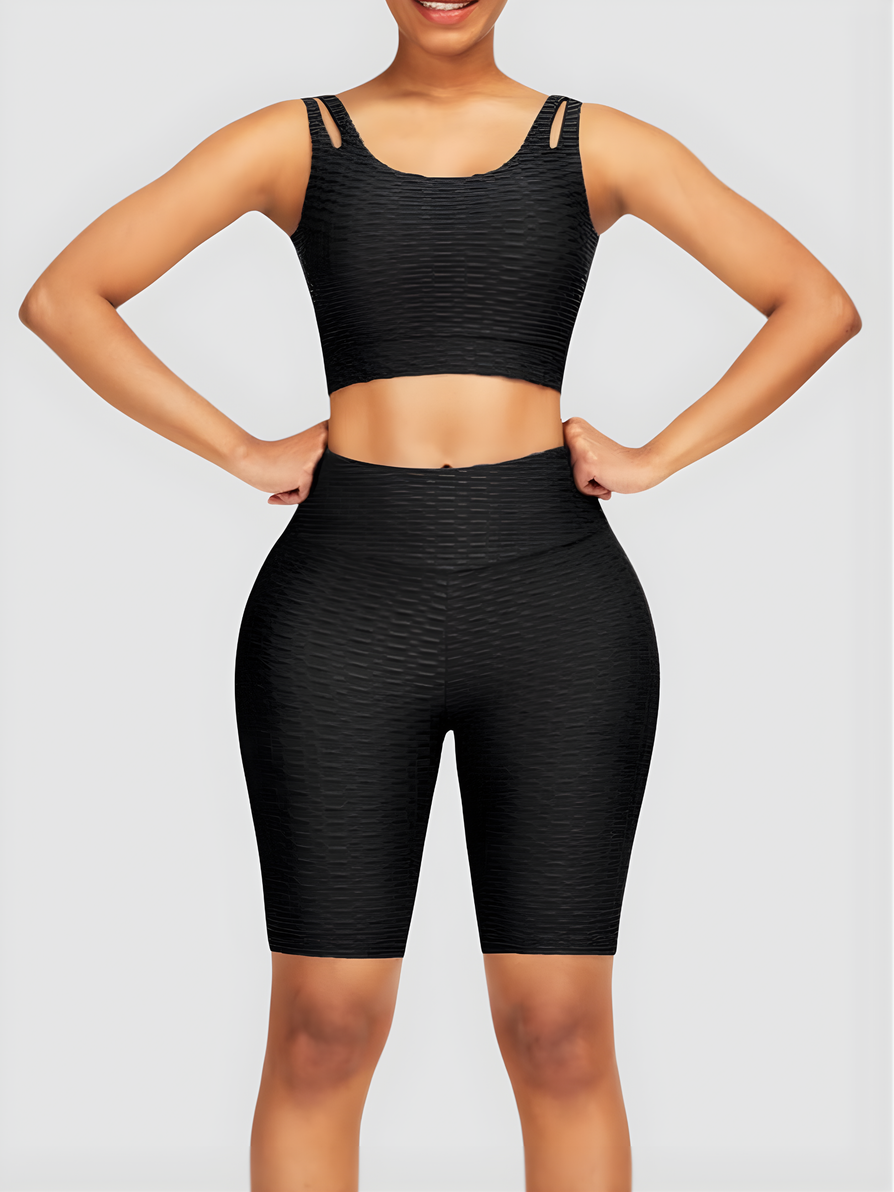 Woman wearing a black activewear set with a matching sports bra and high-waisted tummy control mid-thigh spandex shorts posing with her hands on her hips.