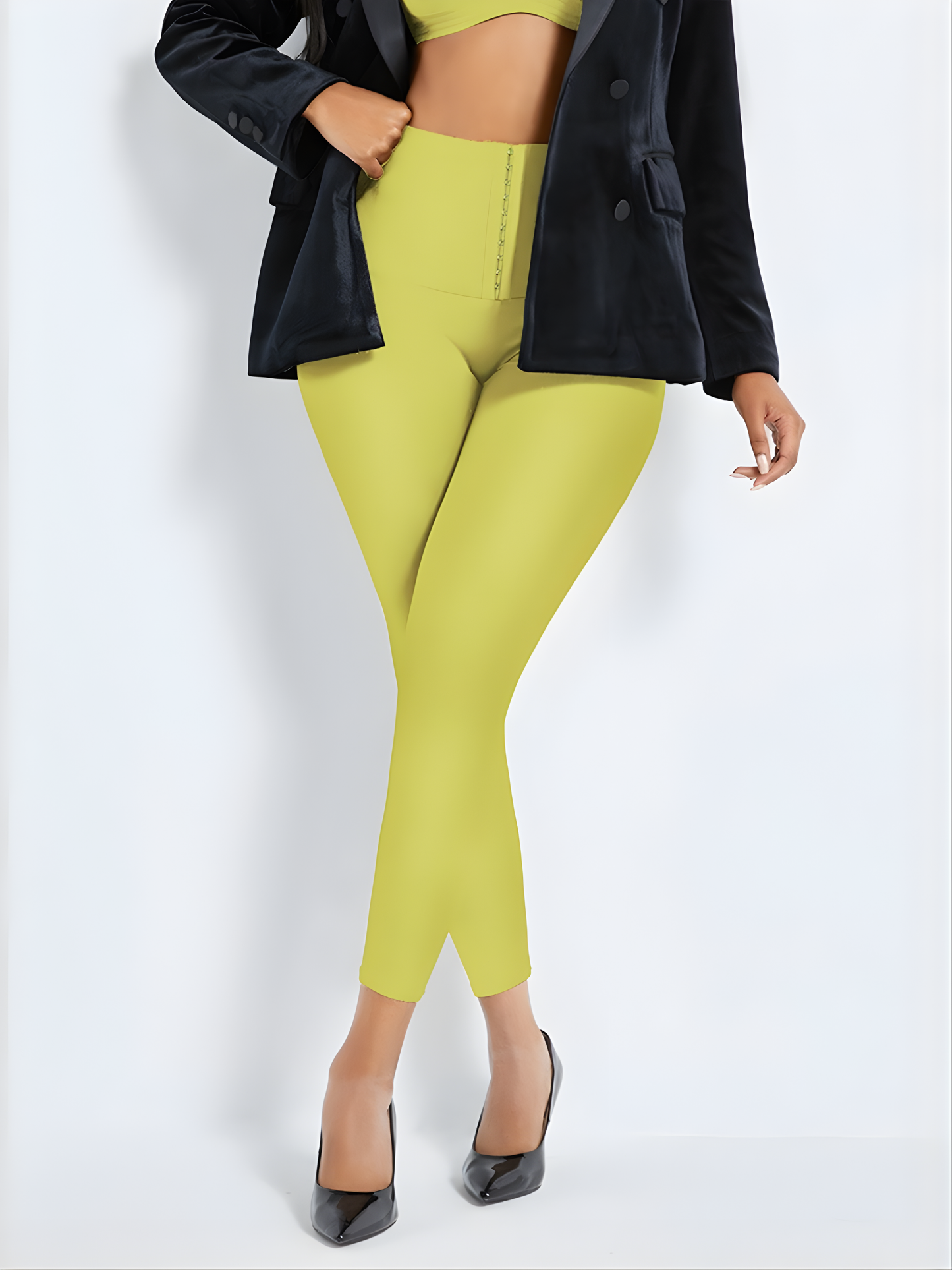 Woman wearing high waisted yellow corset leggings by BodyFlexx Shapewear with a black jacket and black heels.