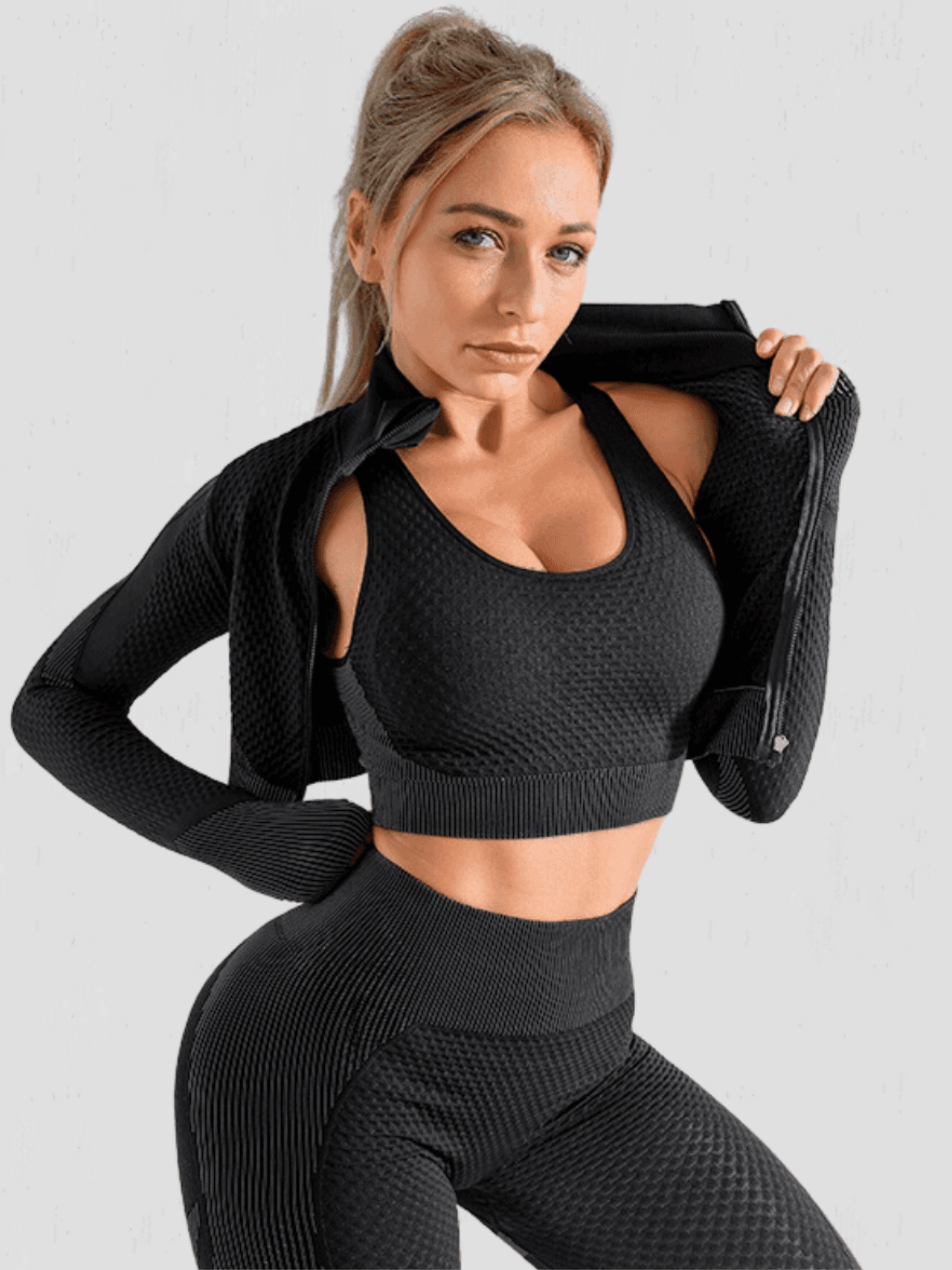 Fitness model posing in a black zippered cropped activewear BBL jacket with matching leggings and sports bra by BodyFlexx.