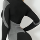 Woman wearing a black and gray color block activewear BBL jacket with matching leggings.