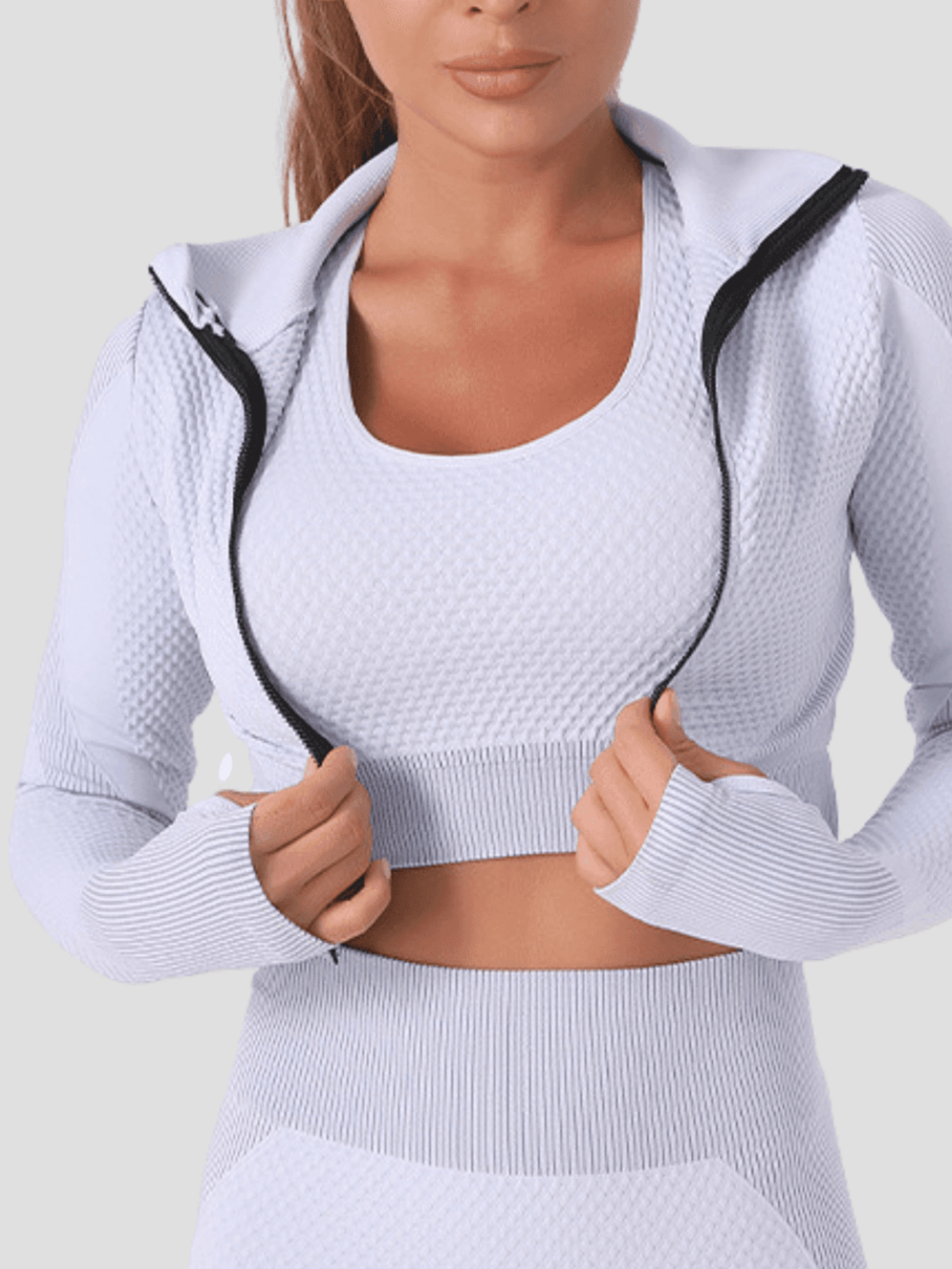 Woman wearing a silver gray zippered activewear BBL jacket with matching leggings.