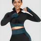Woman wearing a teal and black zippered cropped activewear BBL jacket with matching leggings.