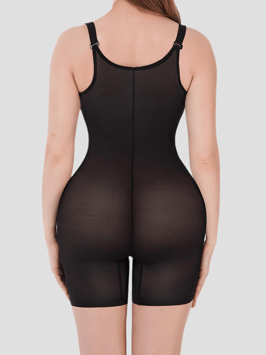 Woman wearing a black sheer open chest bodysuit shapewear standing backwards to show the back view and how it's lifting and shaping her bum.