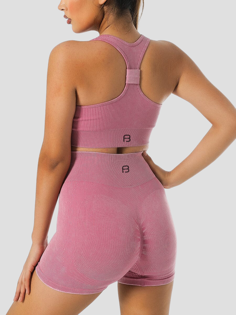 Woman wearing ribbed high-waisted pink activewear shorts and a matching top with the BodyFlexx logo on the back.