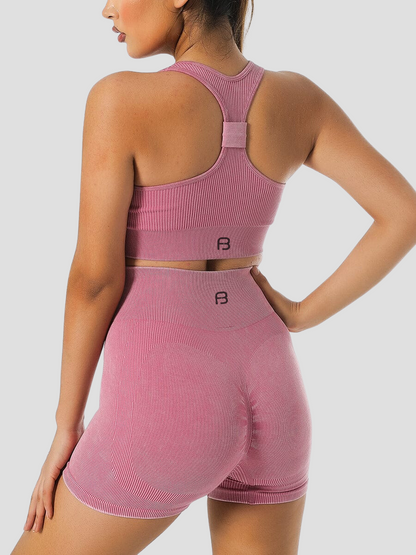 Woman wearing ribbed high-waisted pink activewear shorts and a matching top with the BodyFlexx logo on the back.