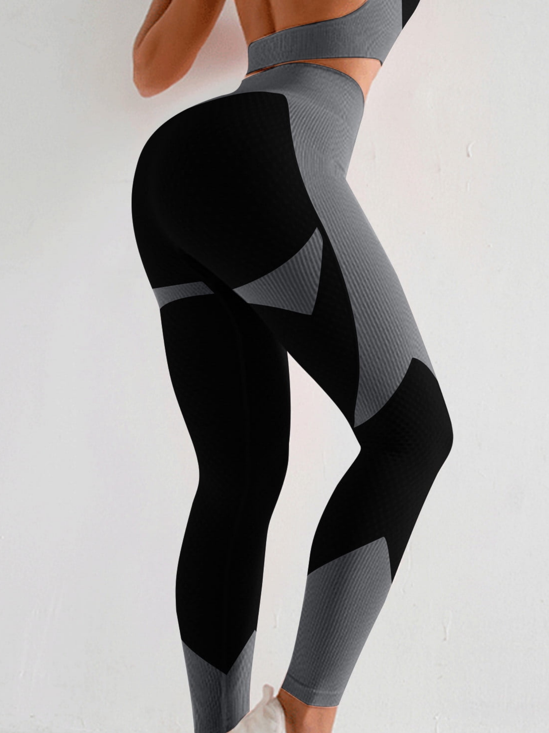 Woman wearing high waisted black and silver gray color block leggings that contour her legs and bum.