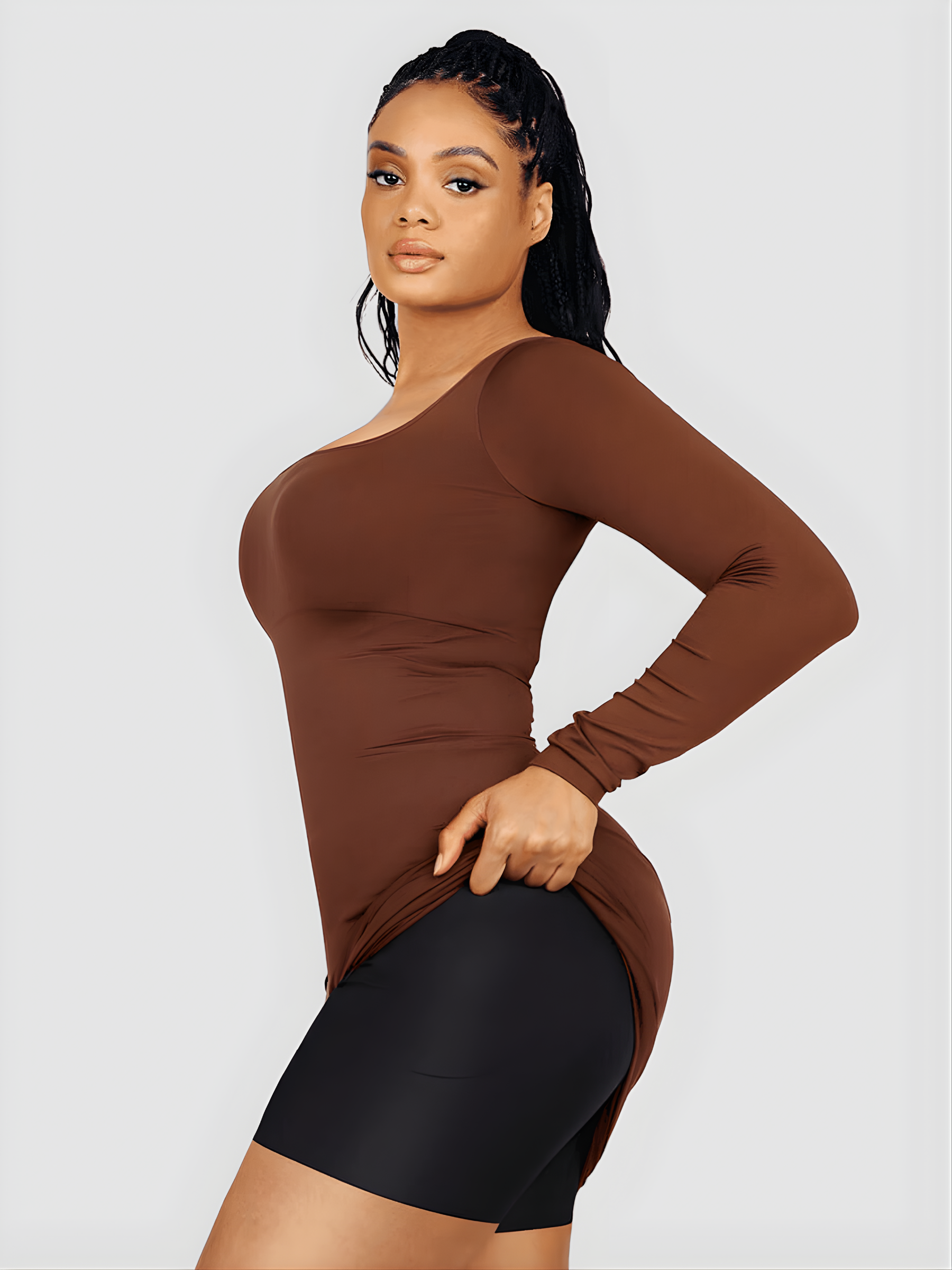 Woman lifting up a brown long-sleeve top dress to show her seamless shapewear with removable hip pads by Bodyflexx.