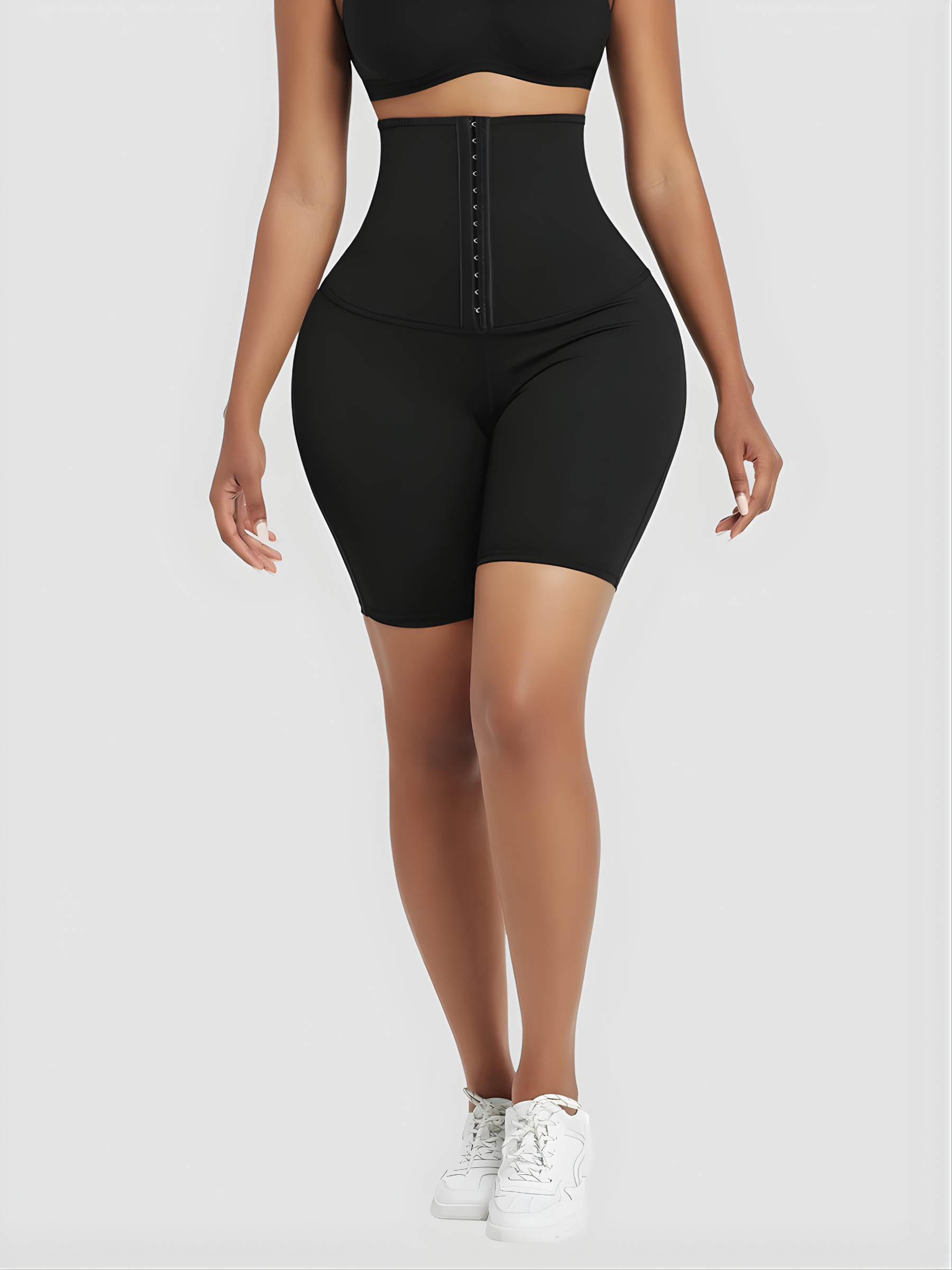 Woman wearing black mid-thigh waist-training sauna shorts with a corset closure.