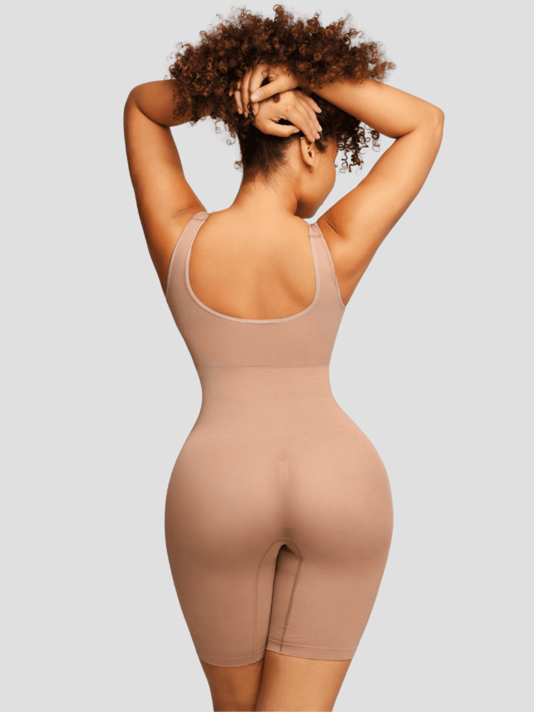 Woman wearing a beige/nude colored mid-thigh shapewear bodysuit showing her backside curves.
