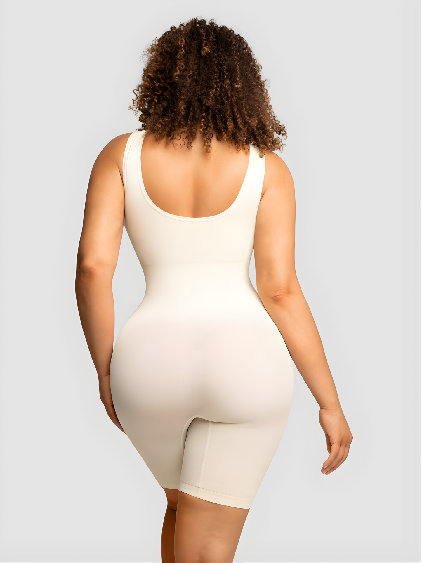 Model wearing an ivory/white colored mid-thigh shapewear bodysuit showing off her cellulite free backside curves.