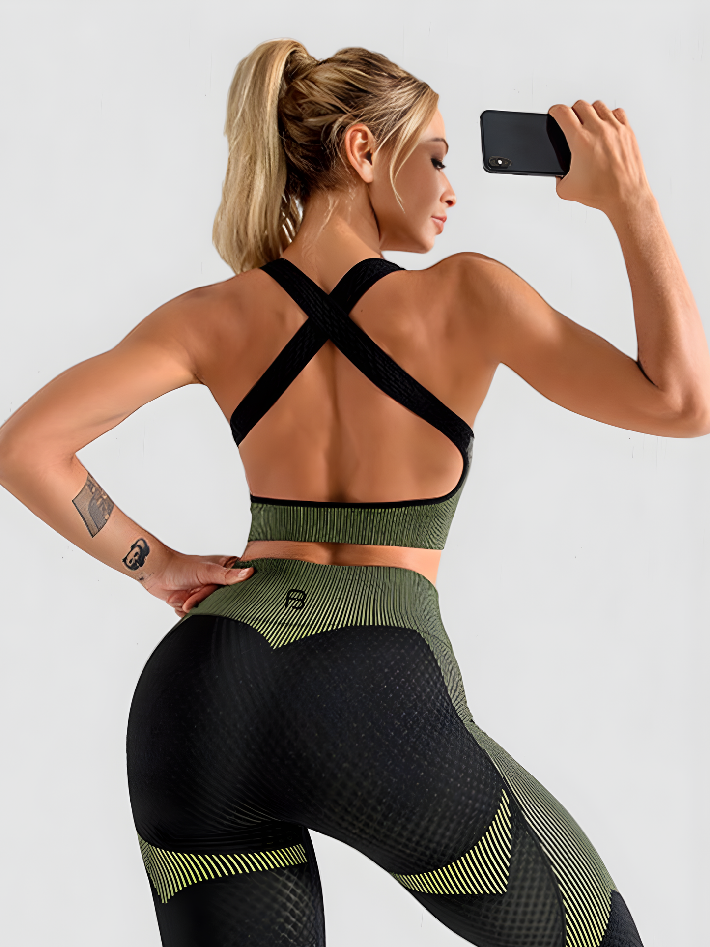 Woman taking a selfie wearing a green and black sports bra with crisscross straps.