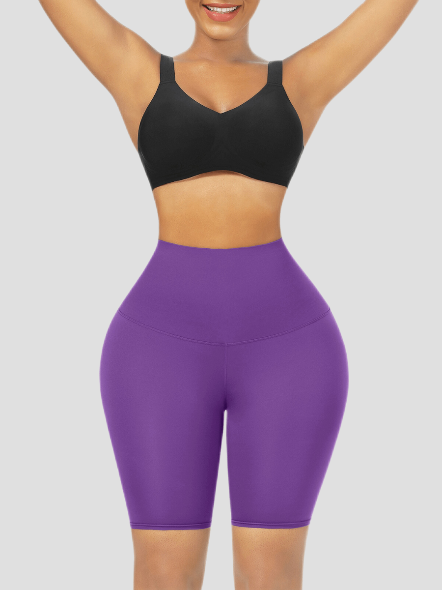 Woman wearing high-waisted purple sauna activewear shorts and a black sports top with her arms in the air smiling after her workout.