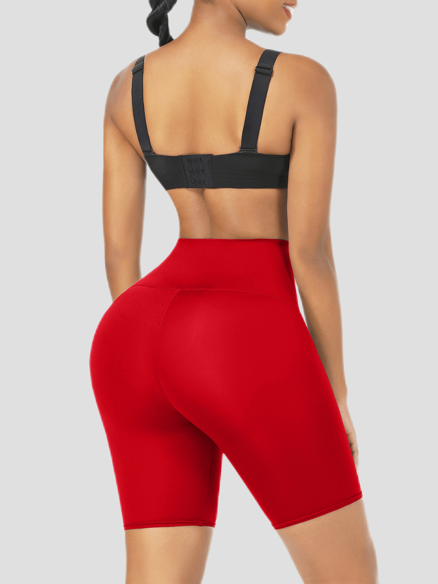Woman posing wearing high-waisted red sauna weight loss shorts and a black activewear top.