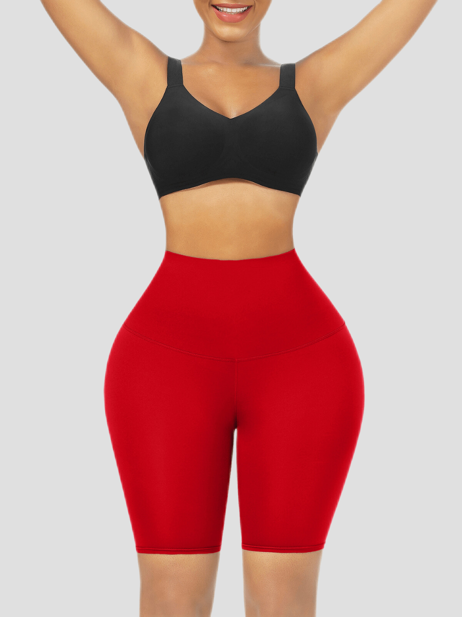 Woman wearing red sauna weight loss shorts and a black activewear top with her hands in the air smiling after a great workout.