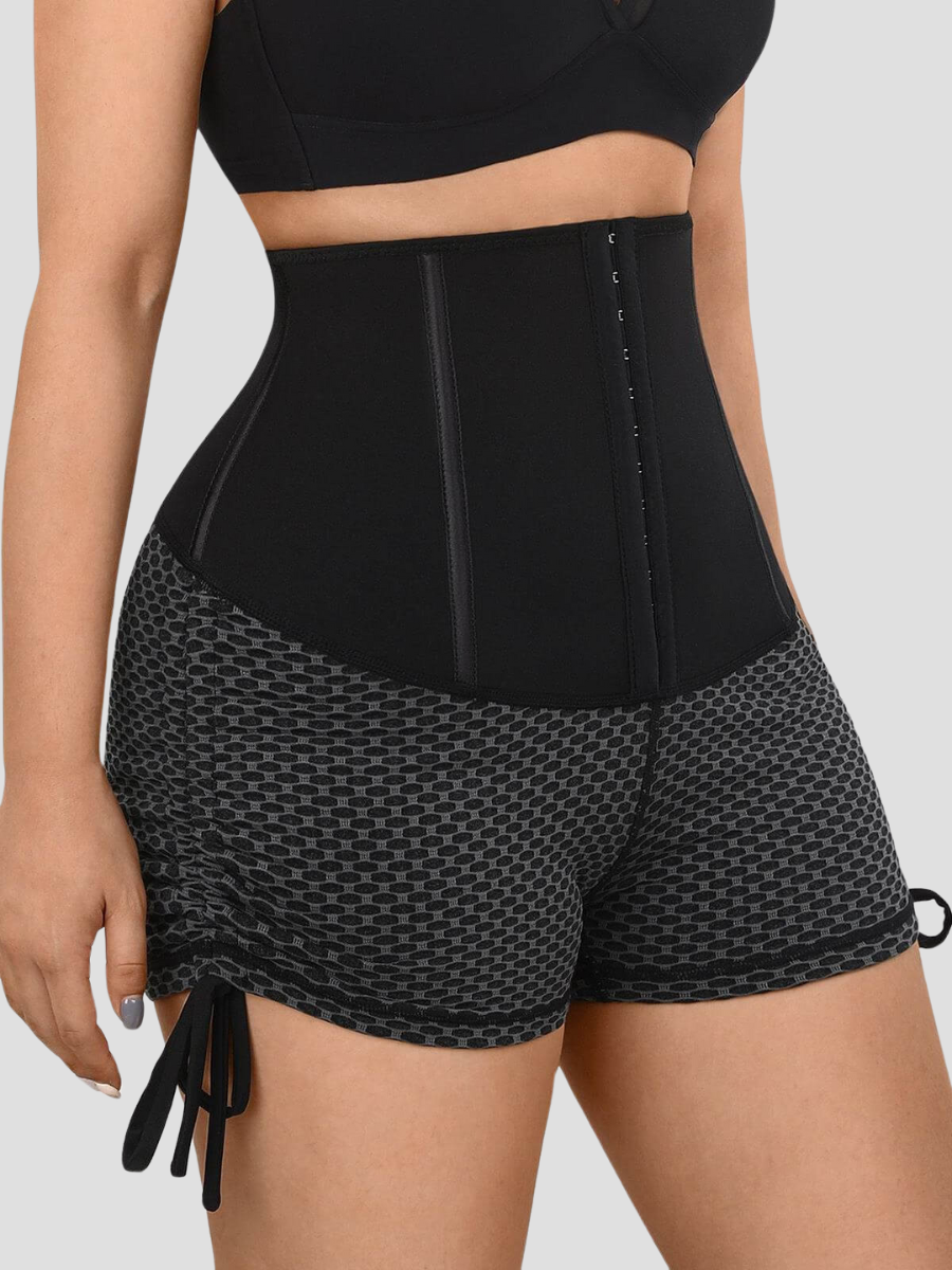 Woman wearing neoprene-lined sauna activewear shorts for weight loss with a black and gray honeycomb pattern and a corset-style hook-and-eye closure.