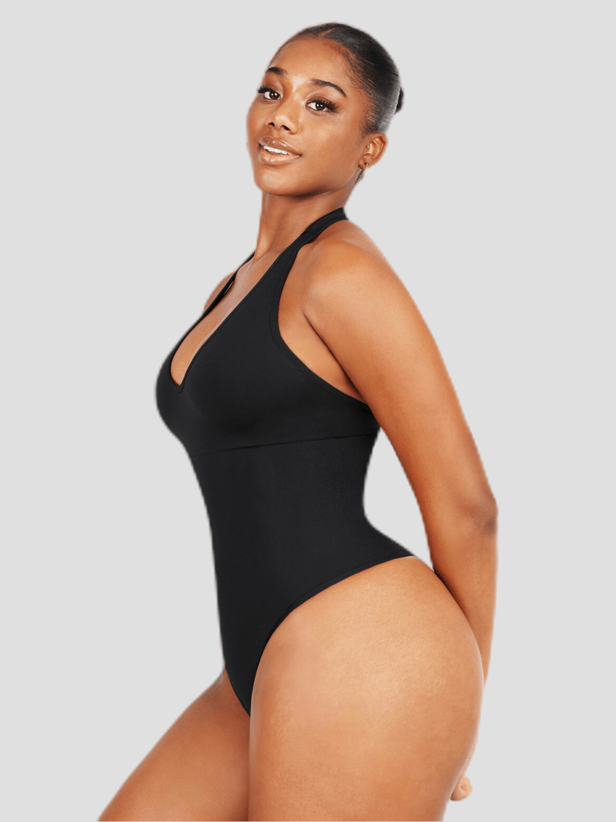 Woman posing wearing a black halter-style shapewear bodysuit with built-in removable bra padding and seamless thong design. She is posing to show off her curves.