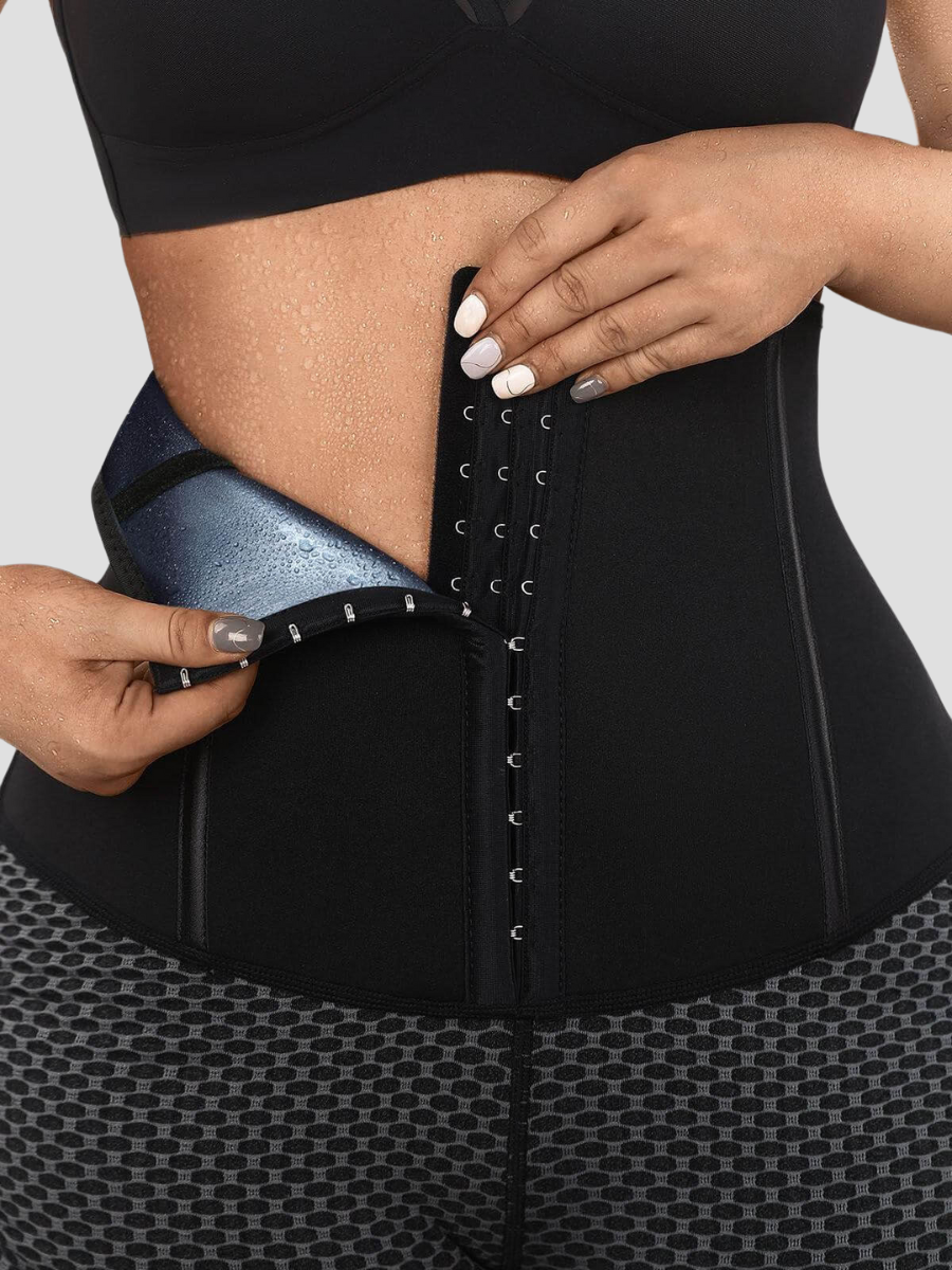 Close up of a woman undoing the waist training corset closure on a pair of black and gray sauna sweat belt lined activewear shorts.