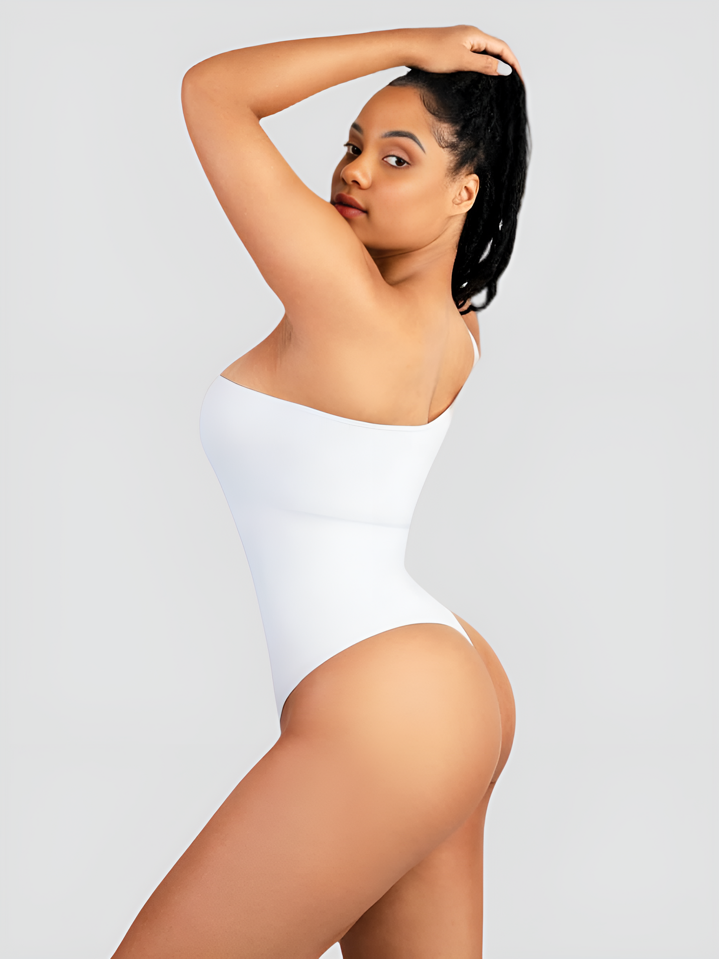 Woman posing wearing a white off-the-shoulder sleeveless shaping bodysuit with built-in shapewear for tummy-control and hourglass curves. She is showcasing the thong design.