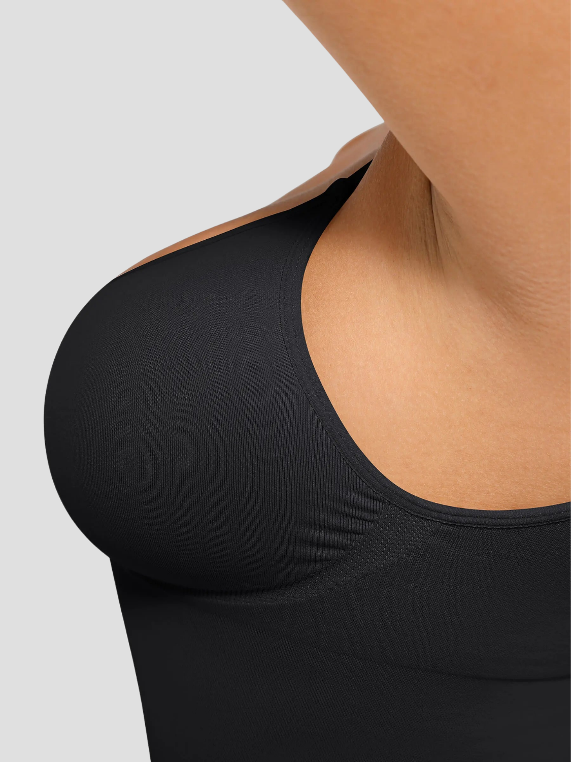 Woman wearing a black shapewear camisole with tummy control and adjustable straps, highlighting the bust support.