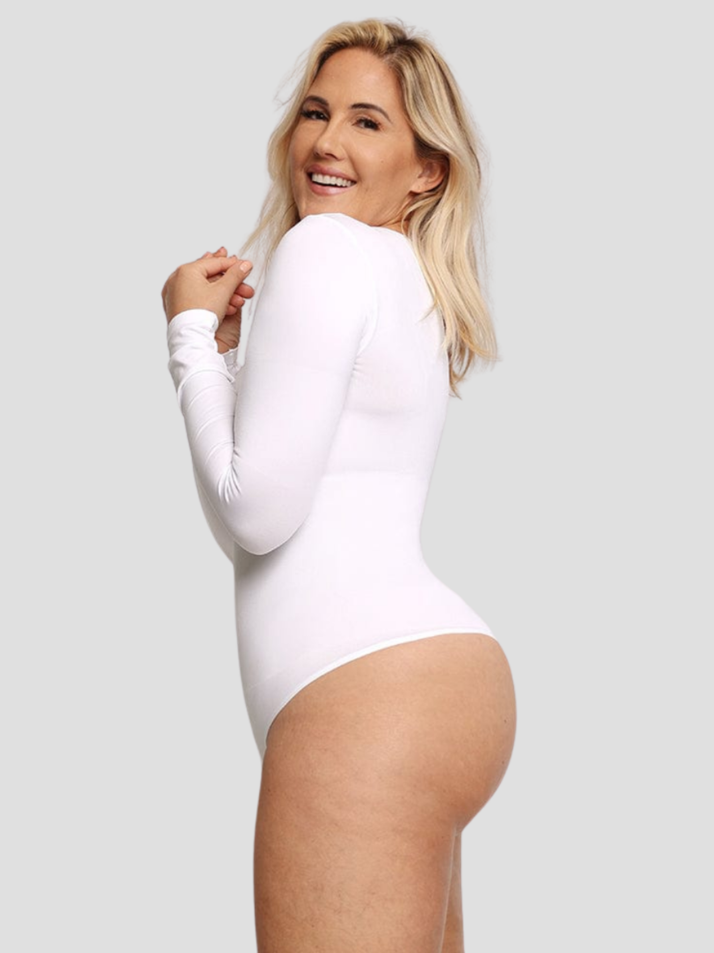 Laughing woman wearing a long-sleeved white bodysuit with built-in shapewear.