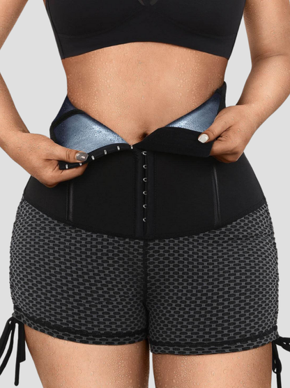 Woman wearing black and gray neoprene-lined sauna activewear shorts showing how to open the corset-style hook-and-eye closure and a sweat-covered tummy.
