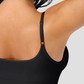 Woman wearing a black shapewear camisole with tummy control and adjustable straps.