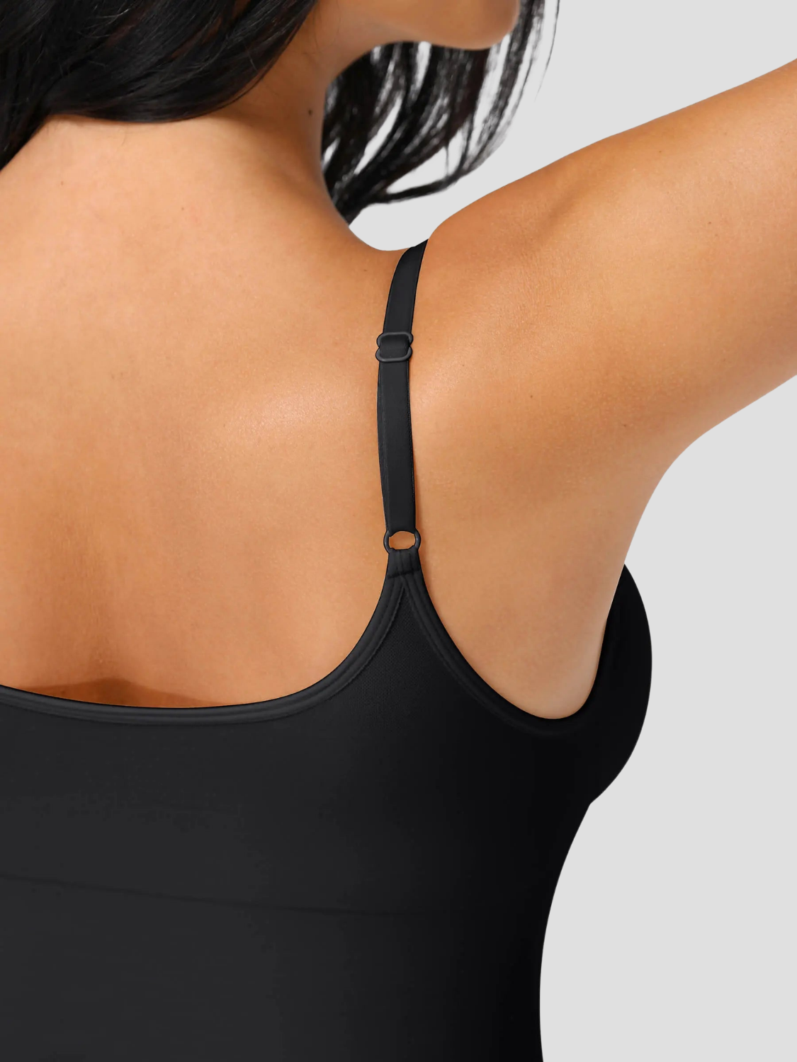 Woman wearing a black shapewear camisole with tummy control and adjustable straps.