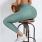Woman wearing teal blue leggings sitting on a bar stool against a white background
